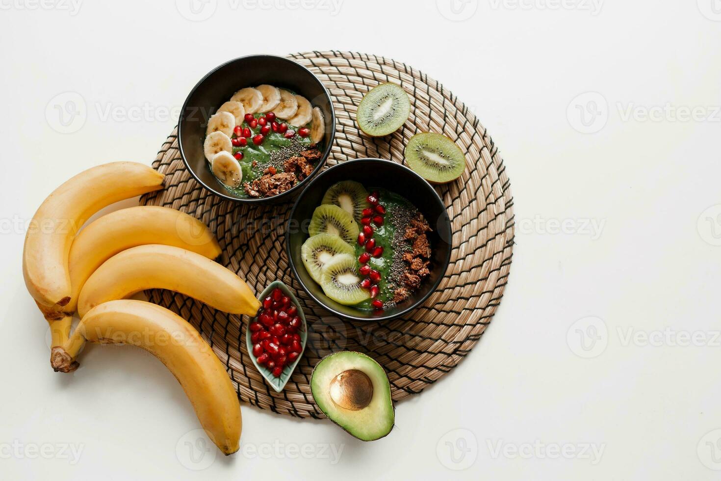 overhead visie Aan bord van groen smoothie kom bekroond met avocado en spinazie , granaatappel zaden en granola. wit achtergrond. foto