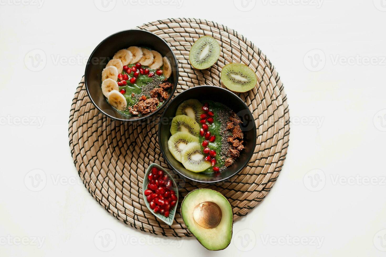 overhead visie Aan bord van groen smoothie kom bekroond met avocado en spinazie , granaatappel zaden en granola. wit achtergrond. foto