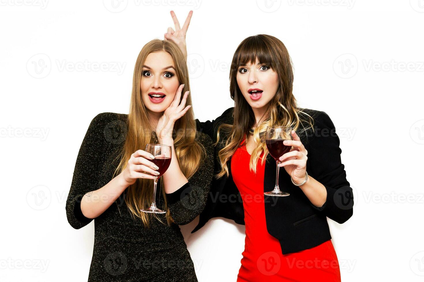 twee gelukkig aantrekkelijk jong Dames, grappig schattig vrienden drinken Liaan en hebben pret over- wit achtergrond. twee meisjes cerebraal nieuw jaar, verjaardag feest. vervelend elegant avond rood jurk. foto