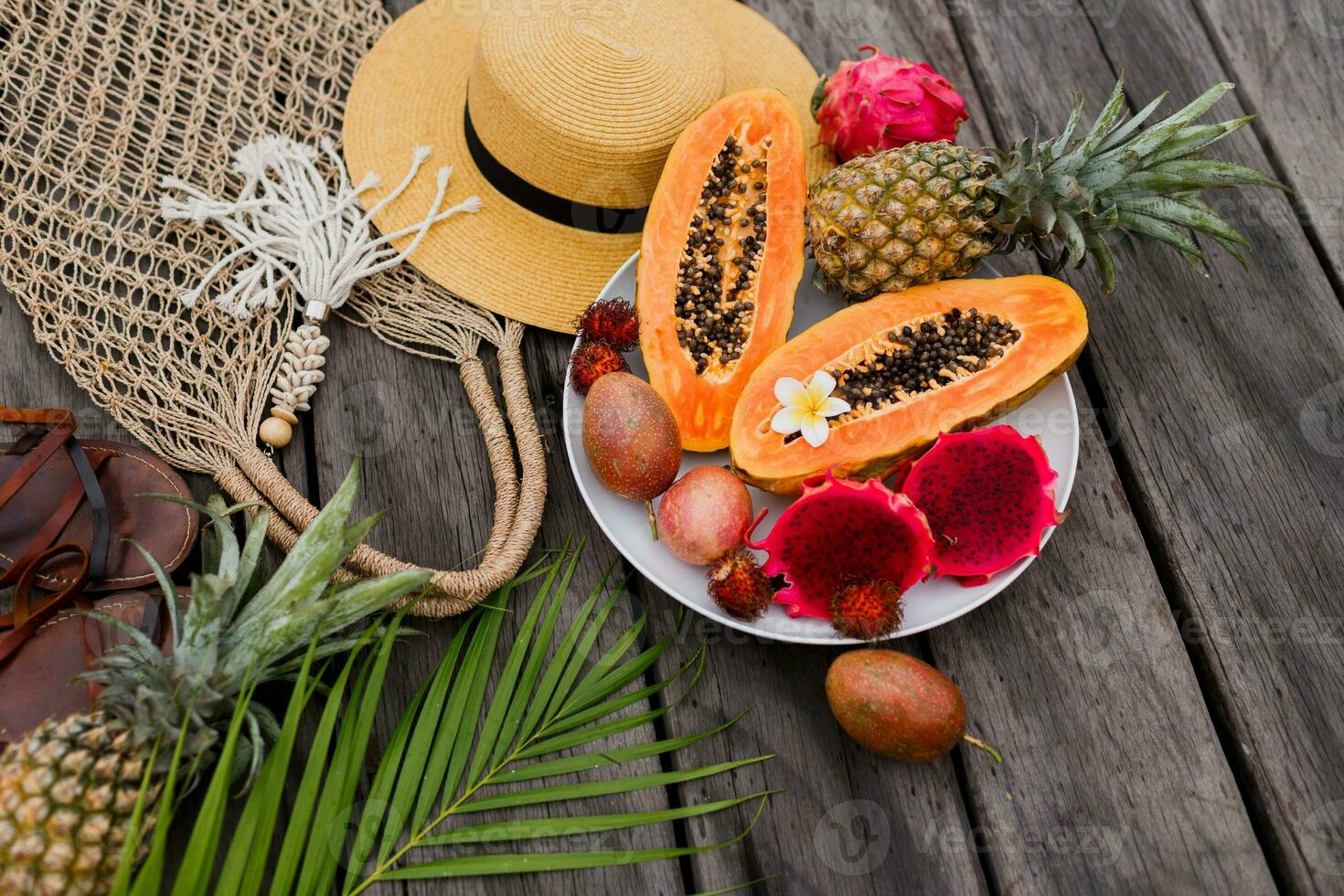 zomer tropisch samenstelling. groen palm bladeren en tropisch fruit Aan hout achtergrond. vlak leggen, top visie. rietje hoed en haken geweven tas. foto