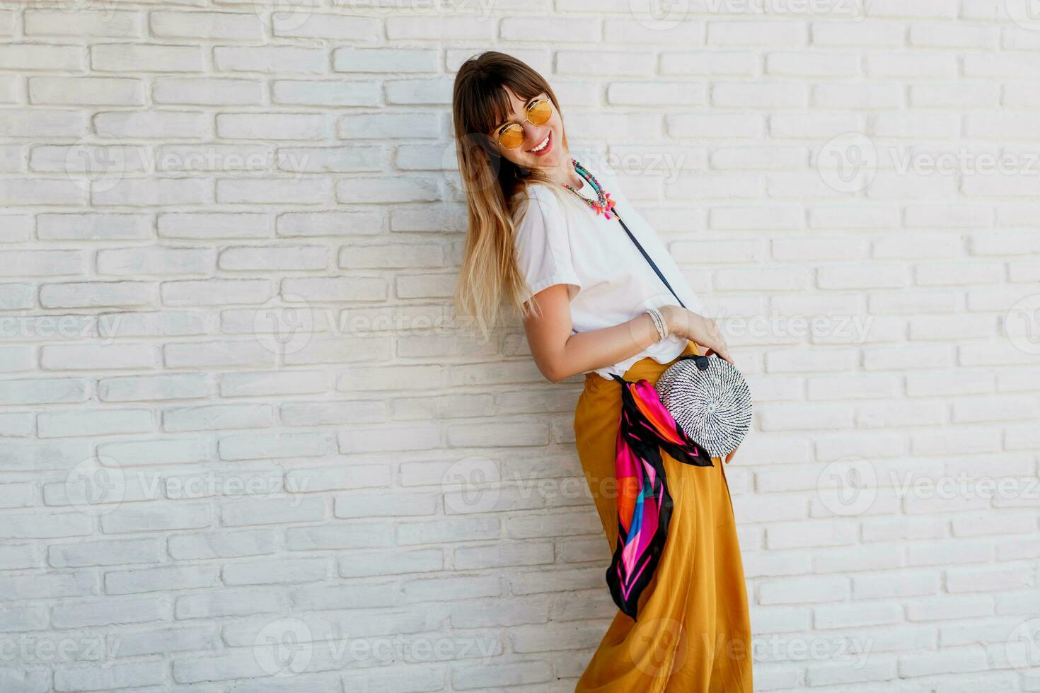 studio schot van zorgeloos vrouw in helder zomer kleding poseren over- wit steen muur achtergrond. Holding ronde rietje zak in Bali stijl. foto