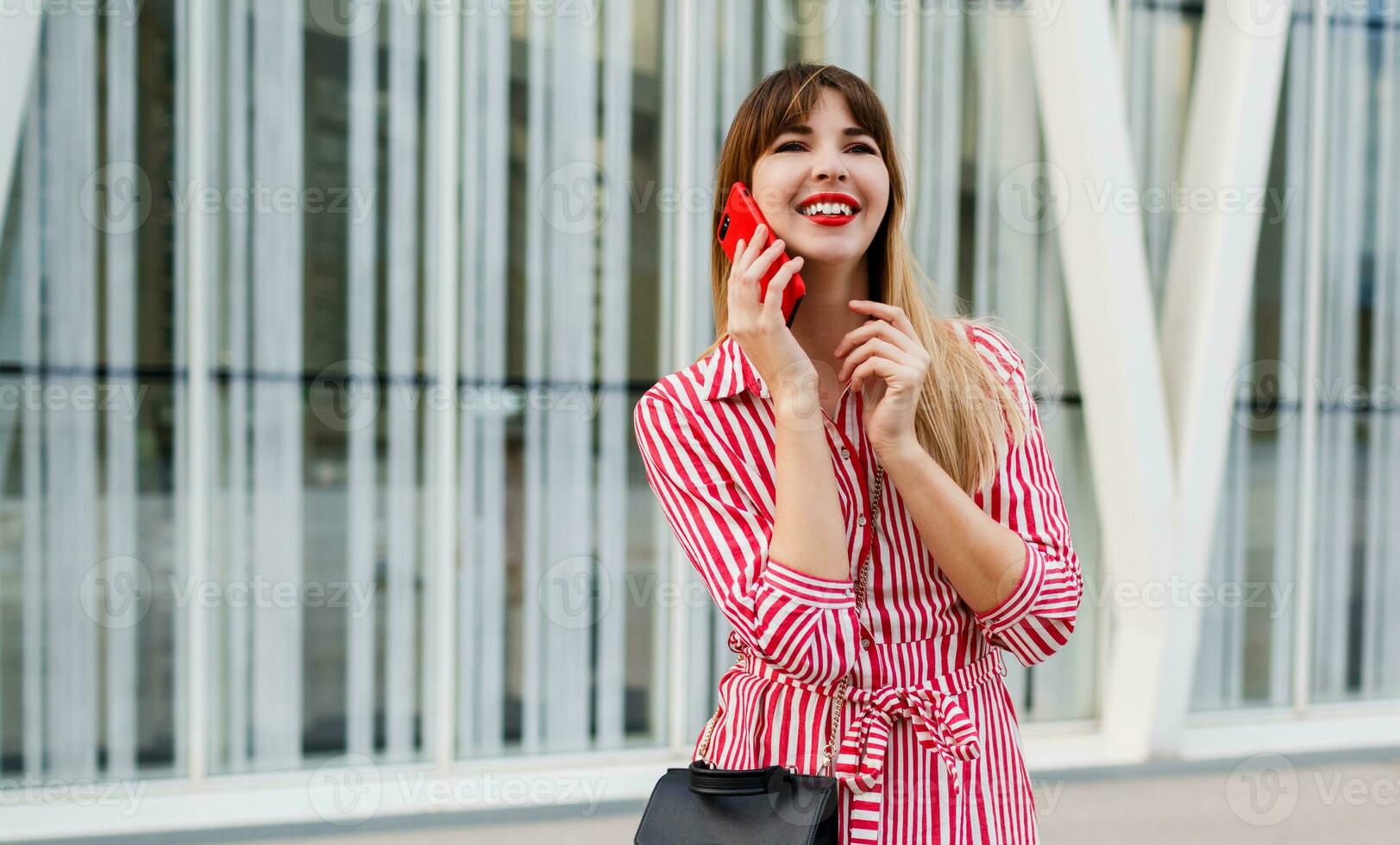 mooi vrouw pratend door mobiel telefoon in rood jurk over- stedelijk achtergrond. foto