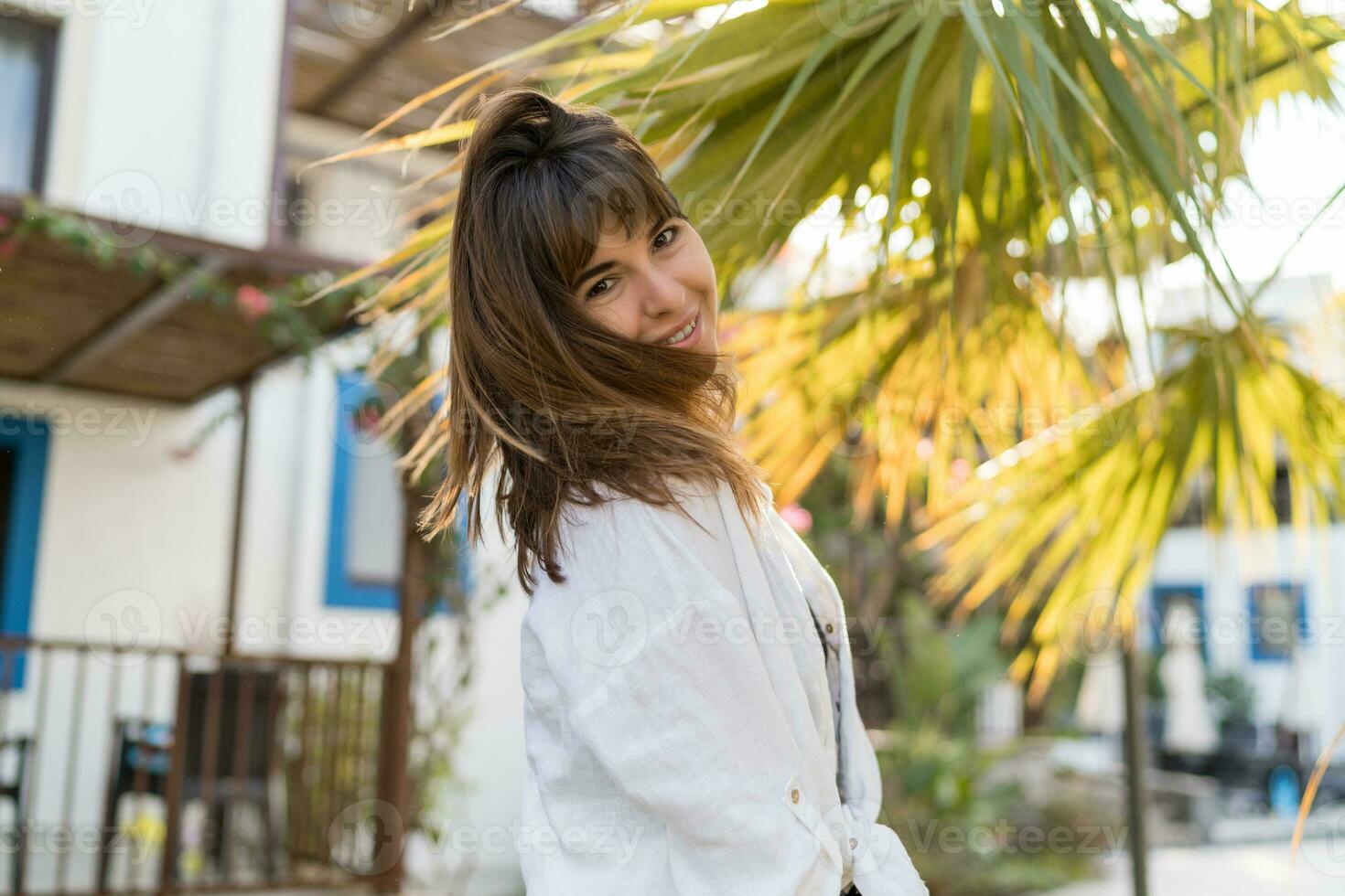 blij brunette vrouw genieten zomer dag. vervelend wit blouse. palm bomen Aan achtergrond. foto