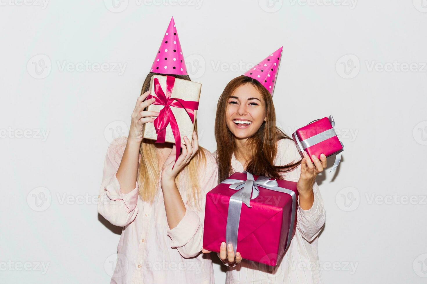 pyjama verjaardag feest. vrienden hebben pret en Holding geschenk dozen. verrassing gezicht, verliet emoties. meisjes vervelend prop partij hoeden. foto