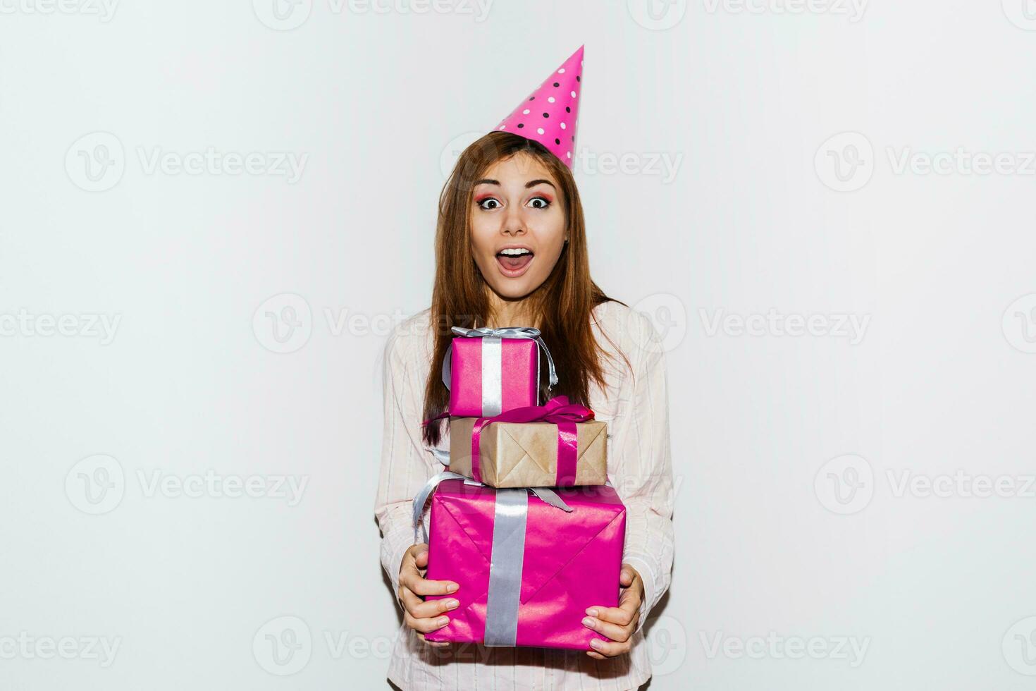 pyjama verjaardag feest. schattig meisje met verrassing gezicht Holding geschenk dozen, vervelend prop partij hoeden. flash portret. wit achtergrond. foto