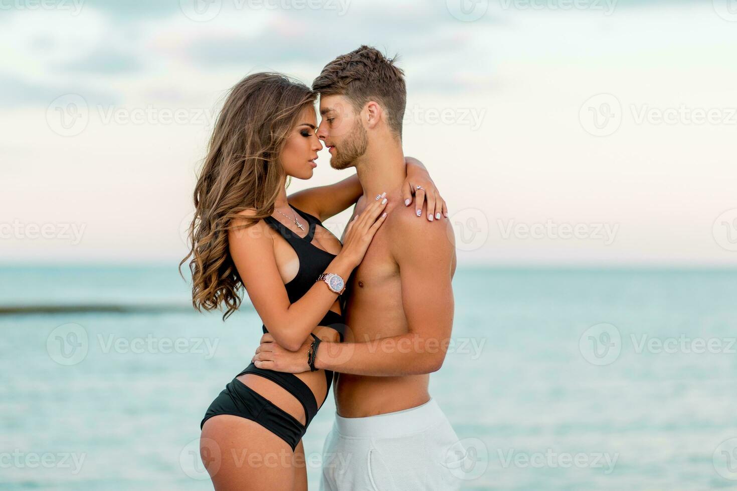 buitenshuis dichtbij omhoog mode portret van mooi sexy paar in liefde knuffels Aan verbazingwekkend tropisch strand, vervelend elegant badmode. foto