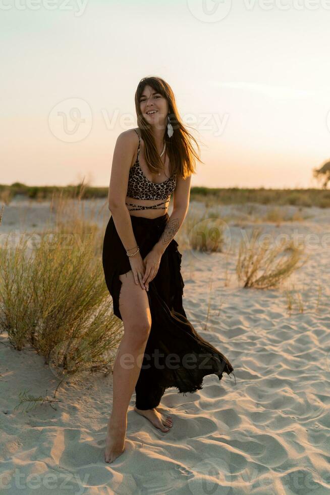 vrolijk brunette vrouw in elegant zomer boho kleding poseren Aan de strand. zonsondergang kleuren. foto