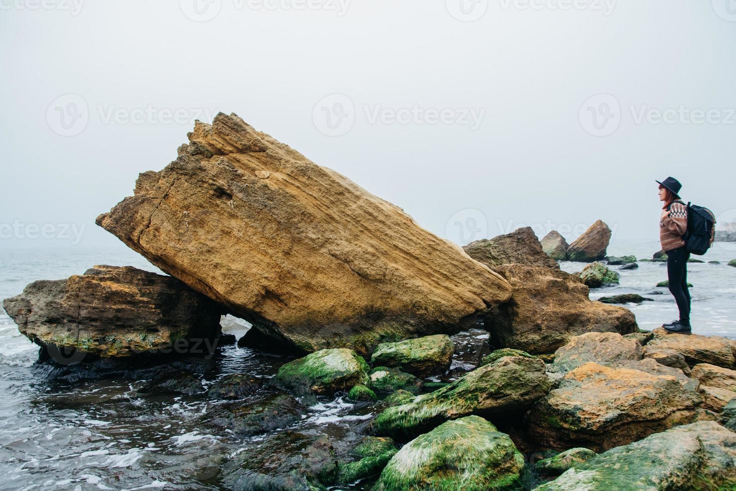 vrouw toerist in hoed met rugzak op rotsen op een achtergrond van zee foto