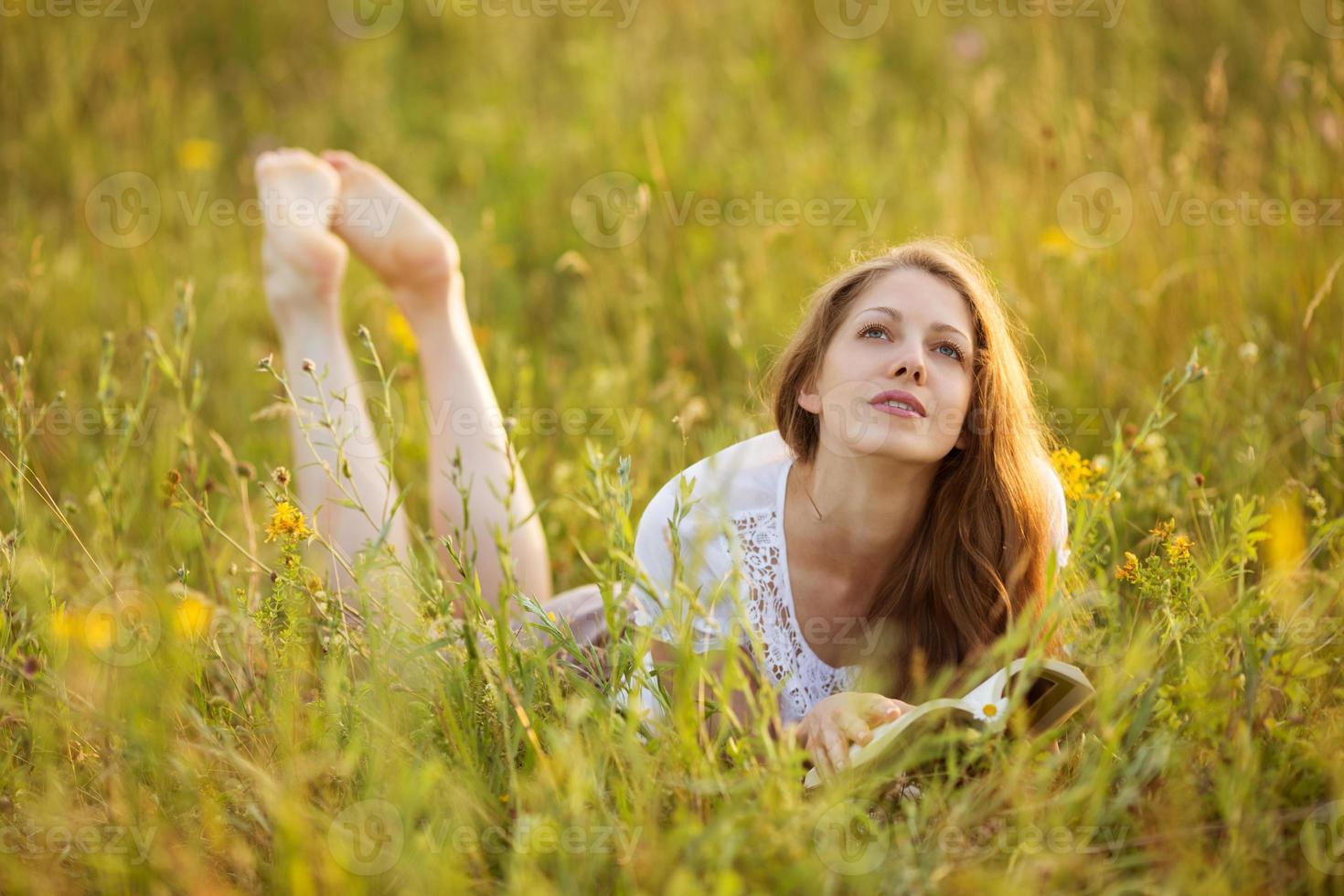meisje met boek ligt in het gras en droomt foto