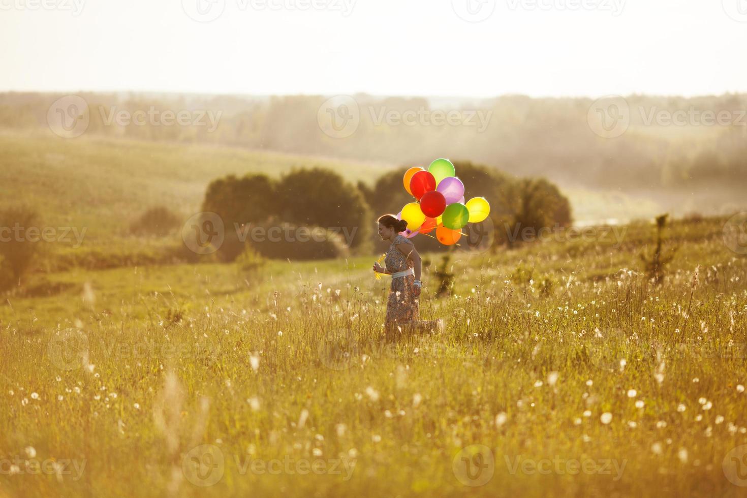 gelukkig meisje met ballonnen die op het veld rennen foto