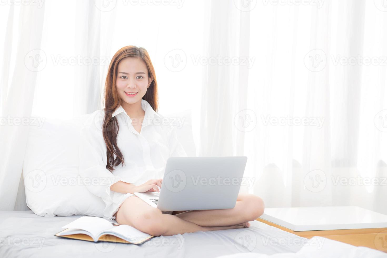 jonge Aziatische vrouw zittend op bed met behulp van laptopcomputer. foto