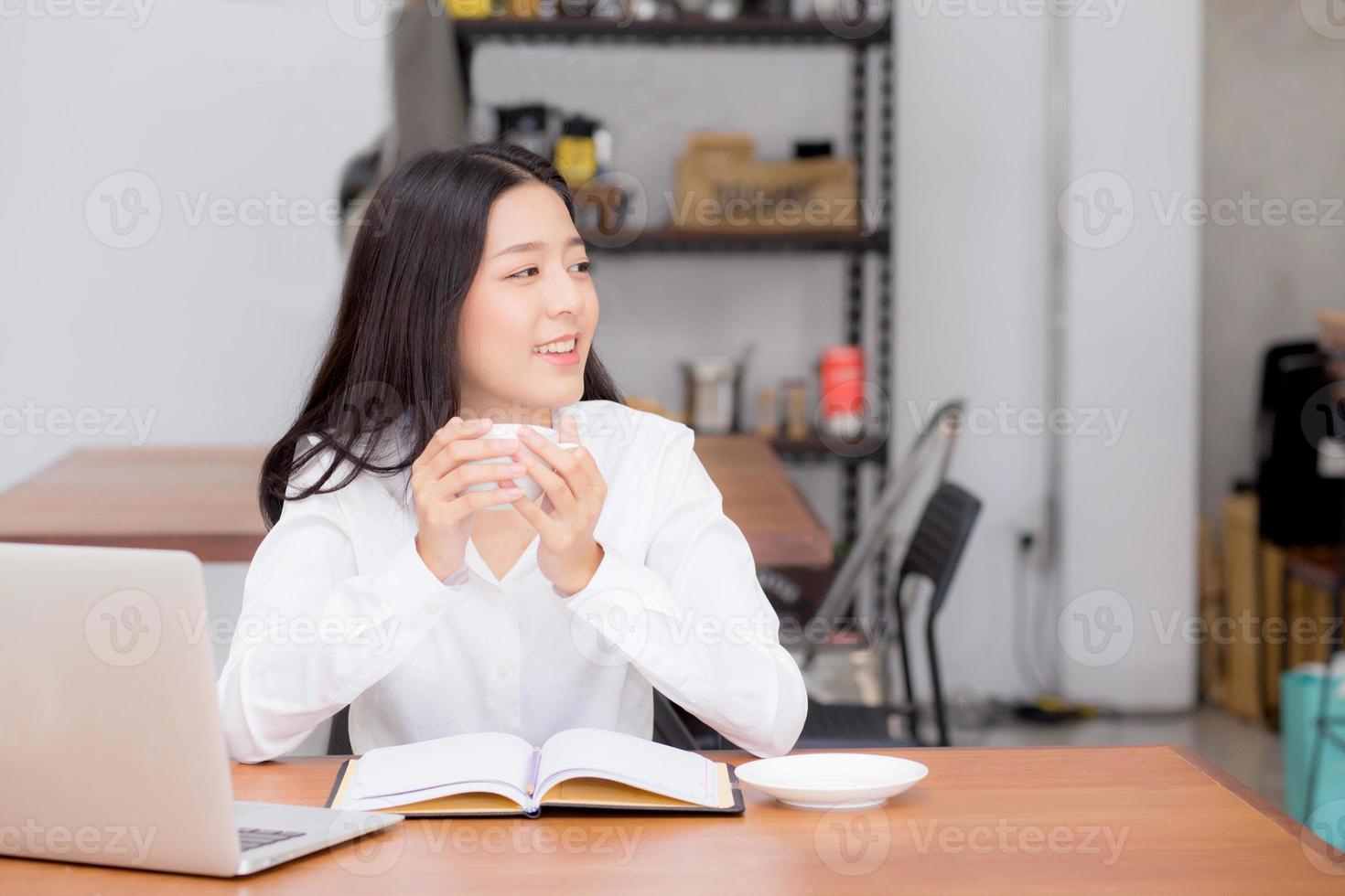 jonge aziatische vrouw die online op laptop werkt en koffie drinkt. foto