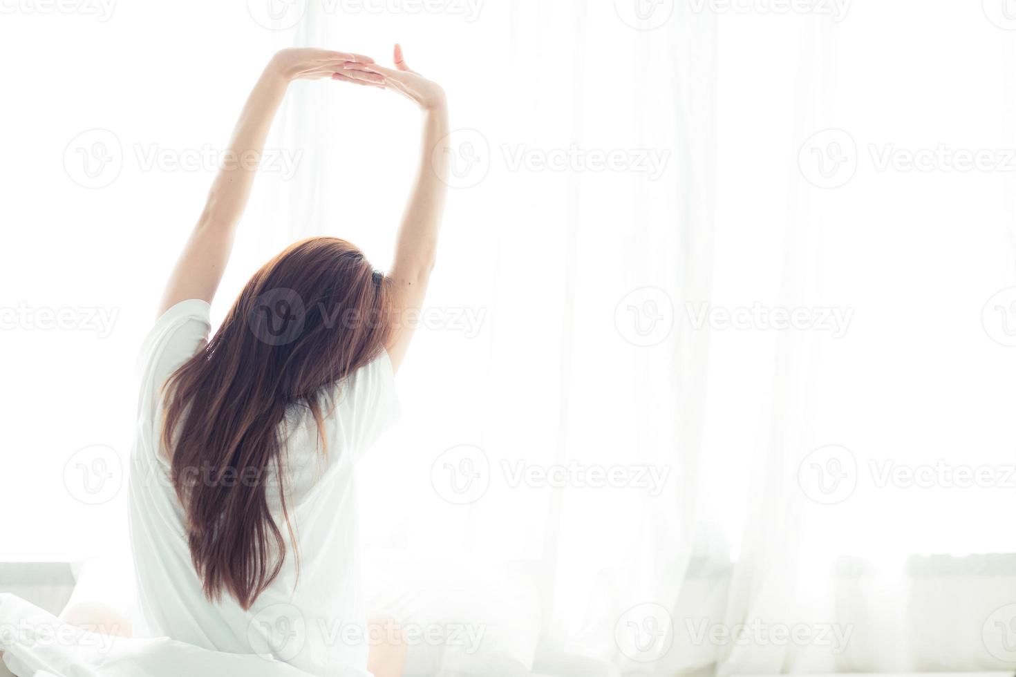 jonge aziatische vrouw strekken en ontspannen in bed na 's ochtends wakker worden. foto