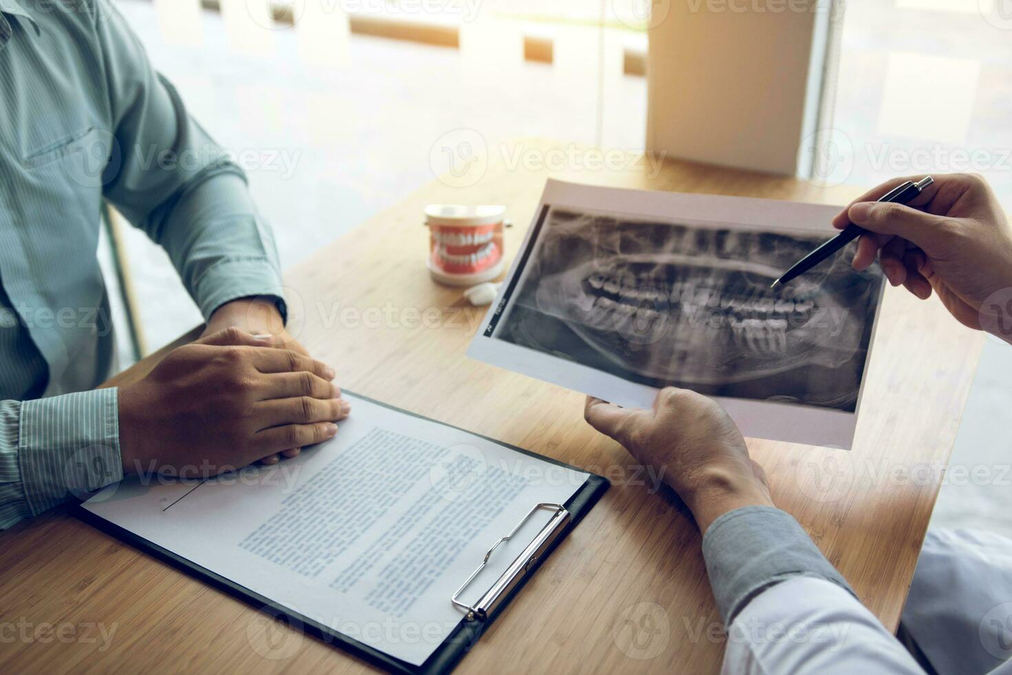 tandarts hand met pen die röntgenfoto wijst en met de patiënt praat over medicatie en chirurgische behandeling. foto