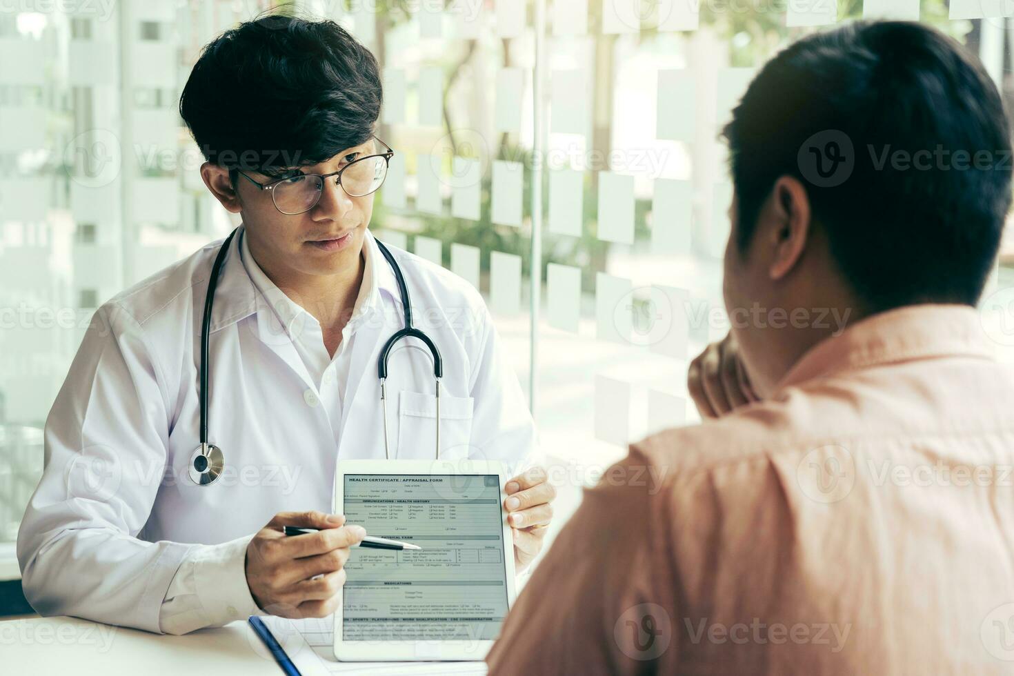 Aziatische arts die de patiënt in de kliniek praat terwijl hij de tablet gebruikt en de toestand van de patiënt en het behandelresultaat uitlegt. foto