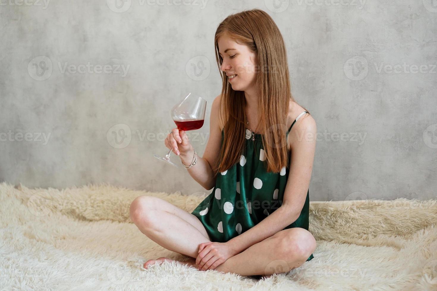meisje in groene pyjama in bed met een glas rode wijn foto