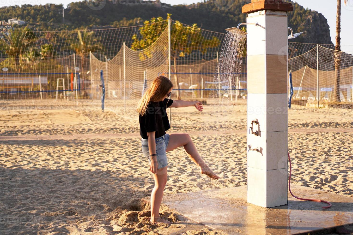 een meisje in korte broek en een zwart t-shirt op het strand bij de douche. foto