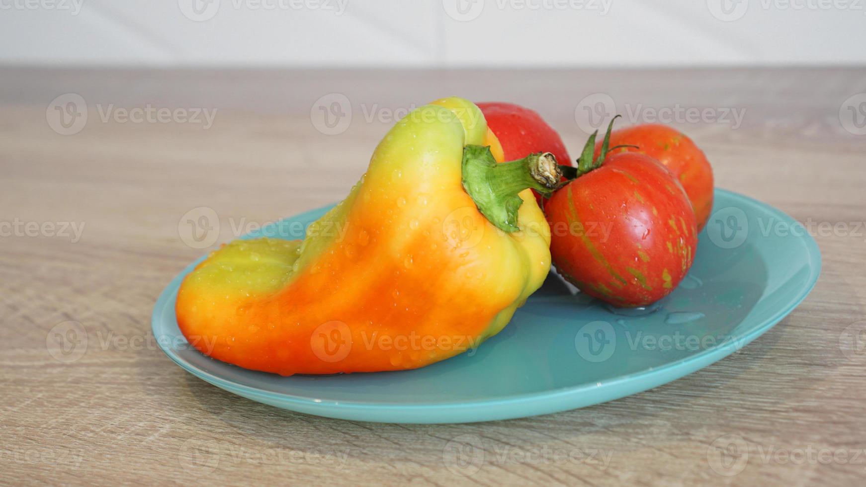 tomaat en peper op een blauw bord op een lichte achtergrond op de keuken foto