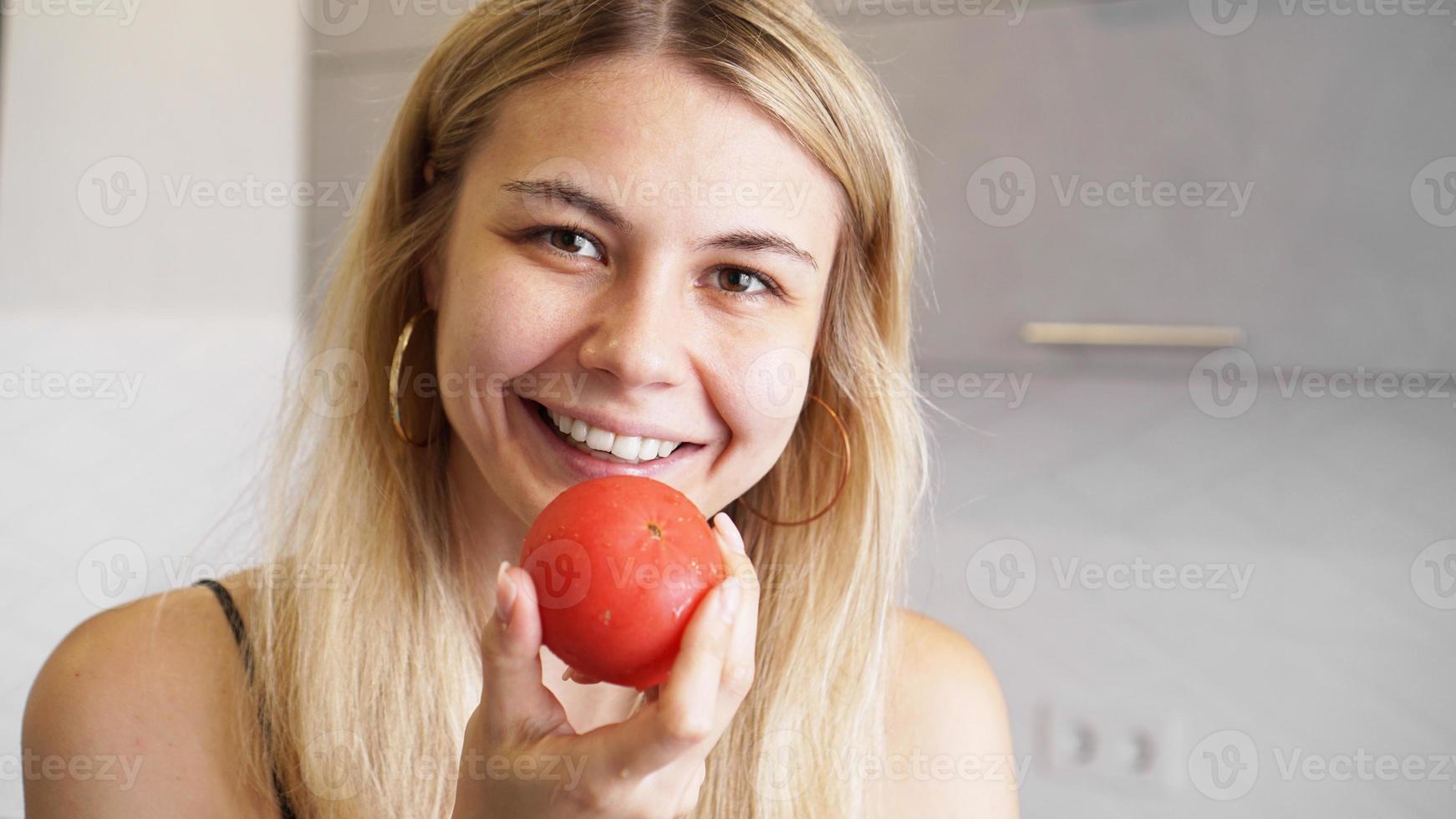 jonge gelukkige vrouw die tomaat vasthoudt en glimlacht foto