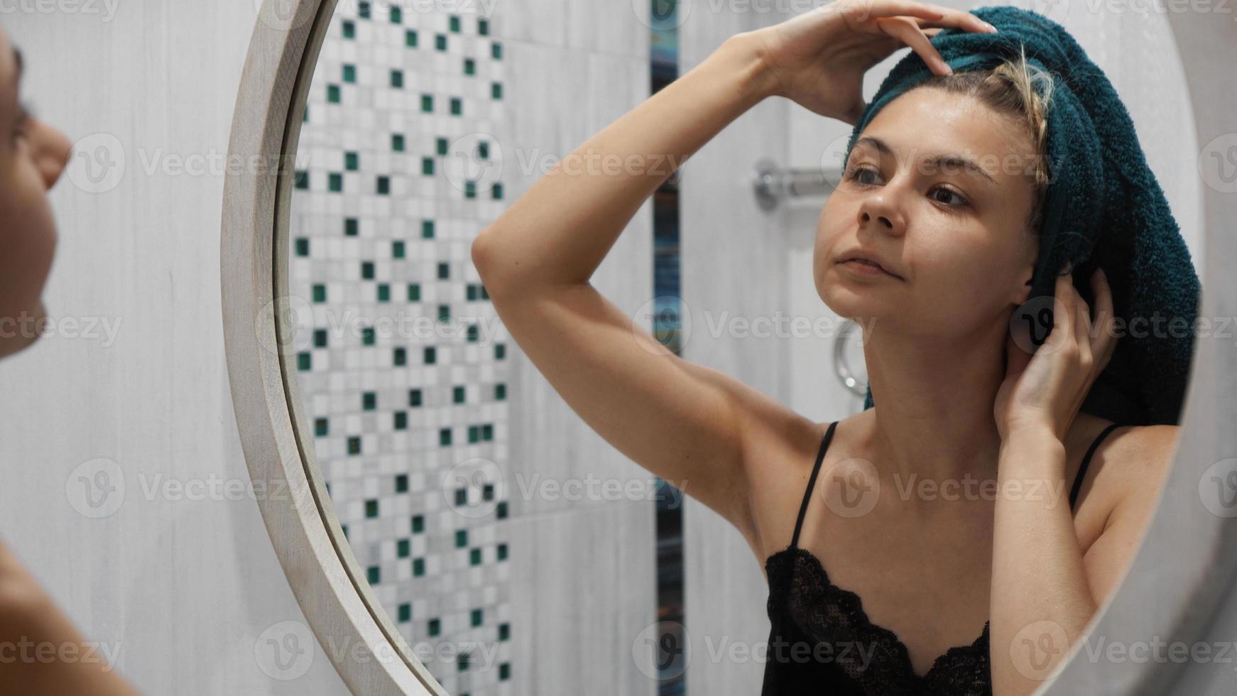 vrouw met een handdoek kijkt in de spiegel in de badkamer foto