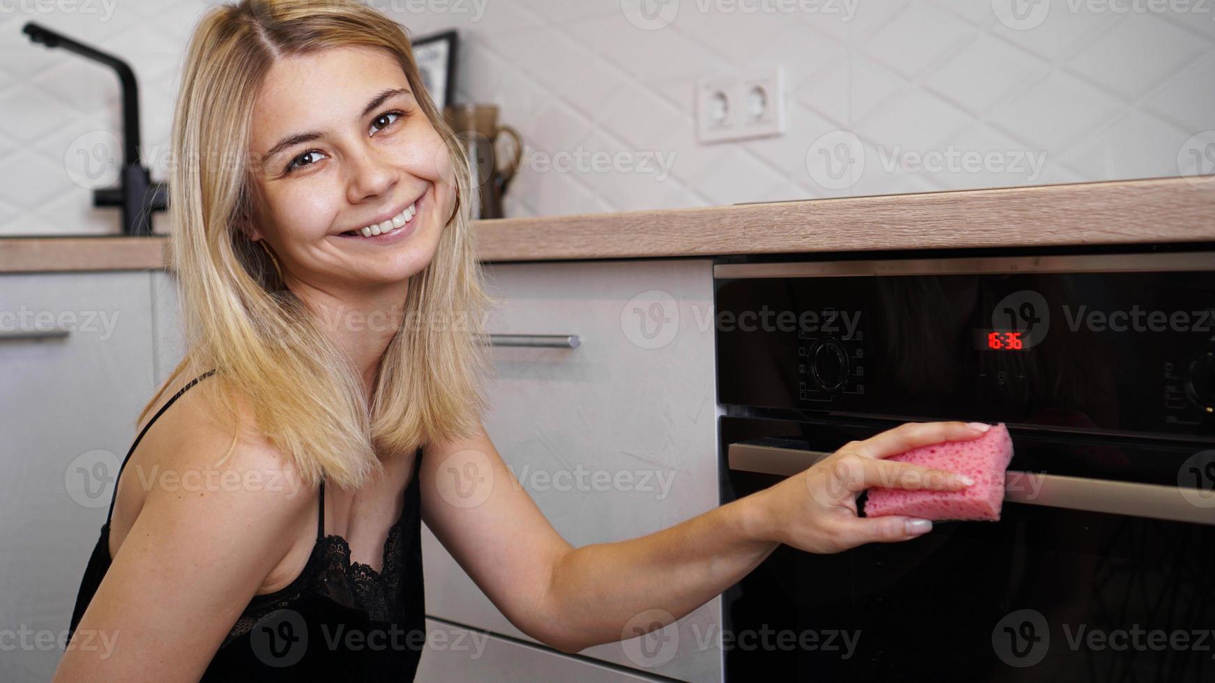 jonge vrouw die oven in de keuken schoonmaakt. foto