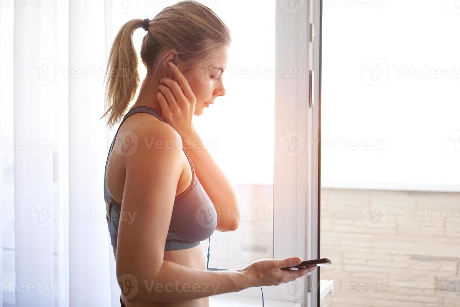 jong mooi sportief meisje staat bij het raam en luistert naar muziek foto