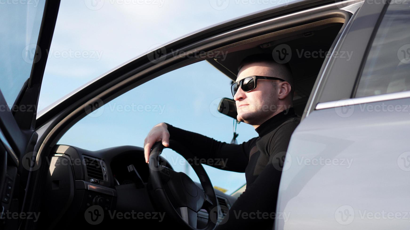 zijaanzicht van zelfverzekerde jonge stijlvolle man in zonnebril in zijn auto foto