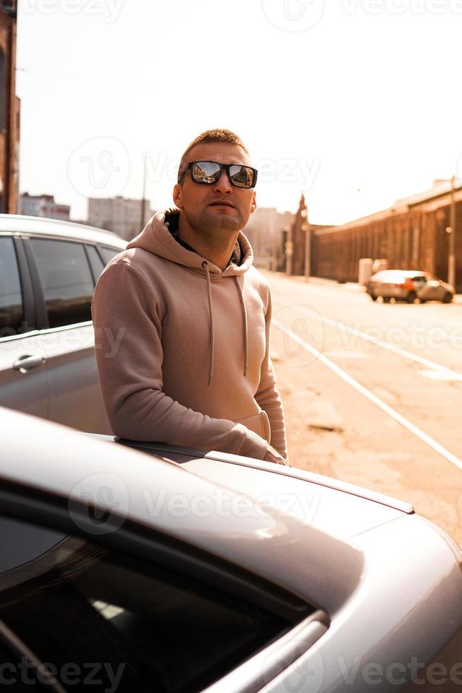 een jonge man naast zijn auto op een zonnige dag op straat foto