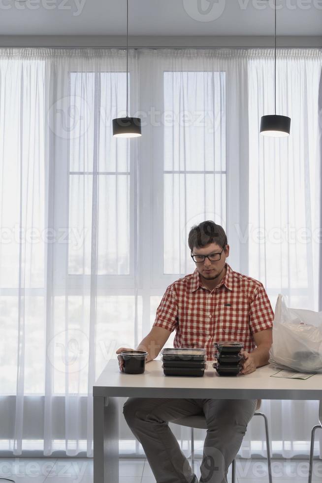 jonge man sorteert voedselbezorgdozen in de moderne keuken foto