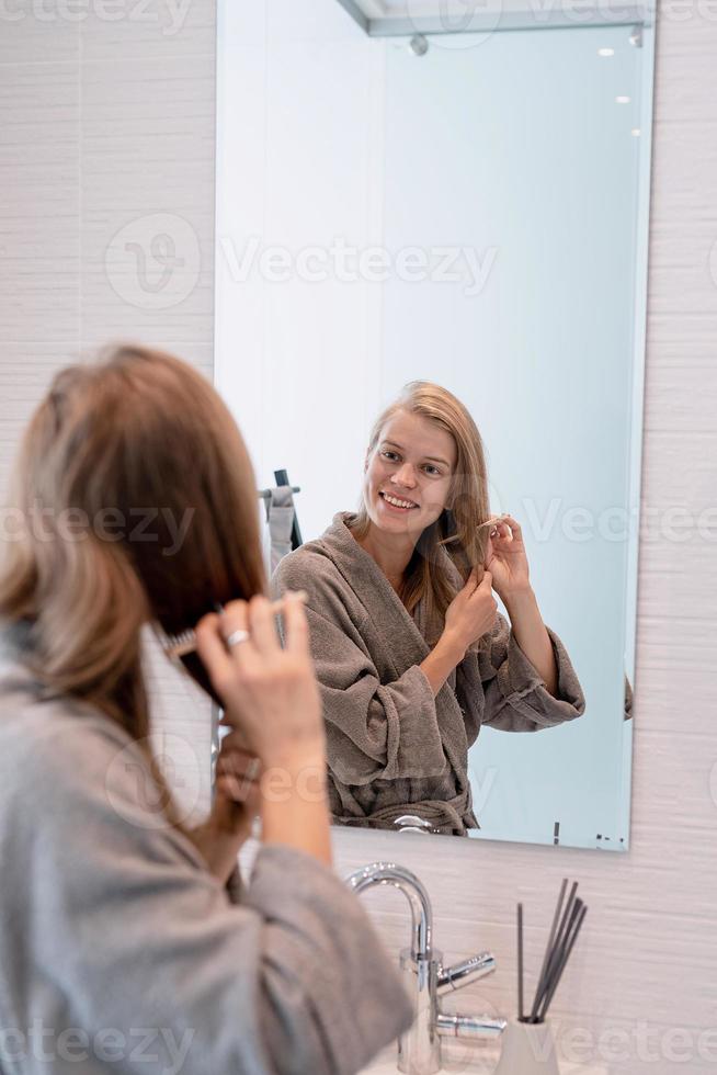 vrouw die haar haar borstelt en glimlacht terwijl ze in de spiegel kijkt foto