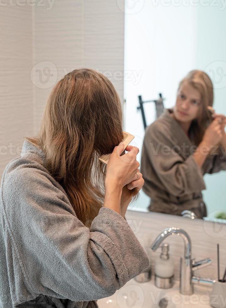 vrouw die haar haar borstelt en glimlacht terwijl ze in de spiegel kijkt foto