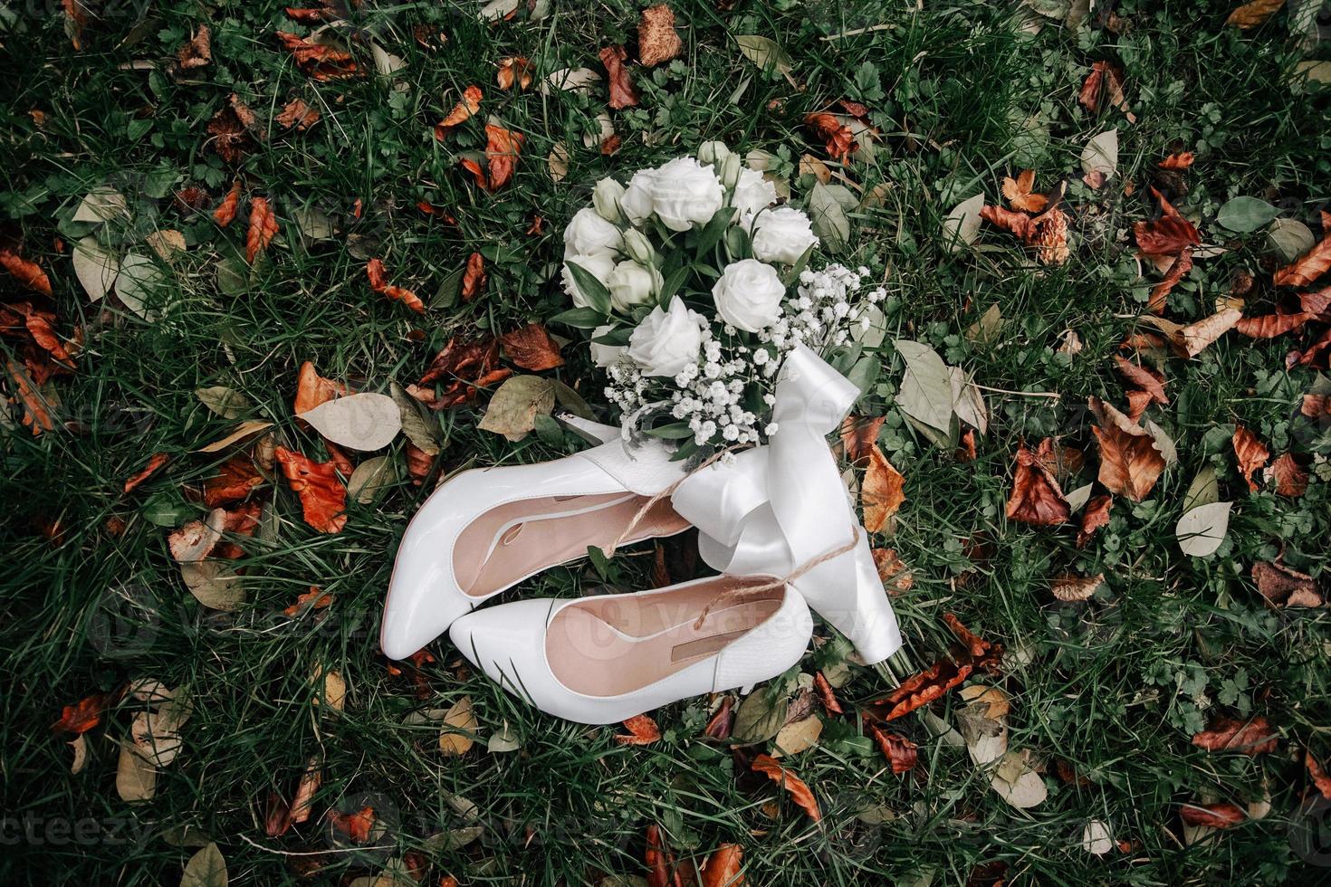 bruidsboeket van witte rozen en schoenen met hoge hakken op een groen gras foto