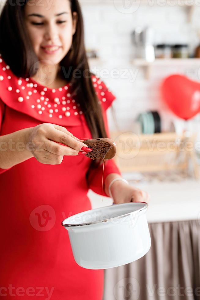 vrouw in rode jurk die valentijnkoekjes maakt in de keuken foto