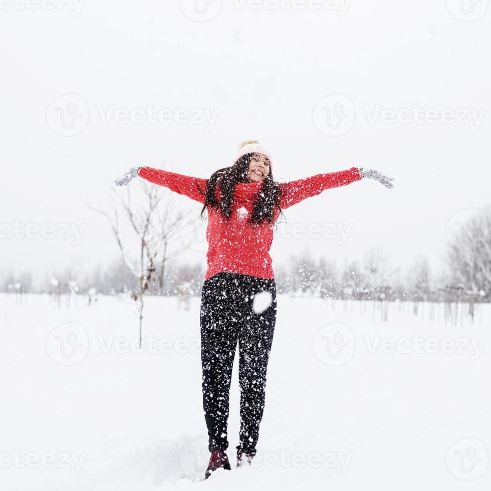 jonge brunette vrouw in rode trui spelen met sneeuw in park foto