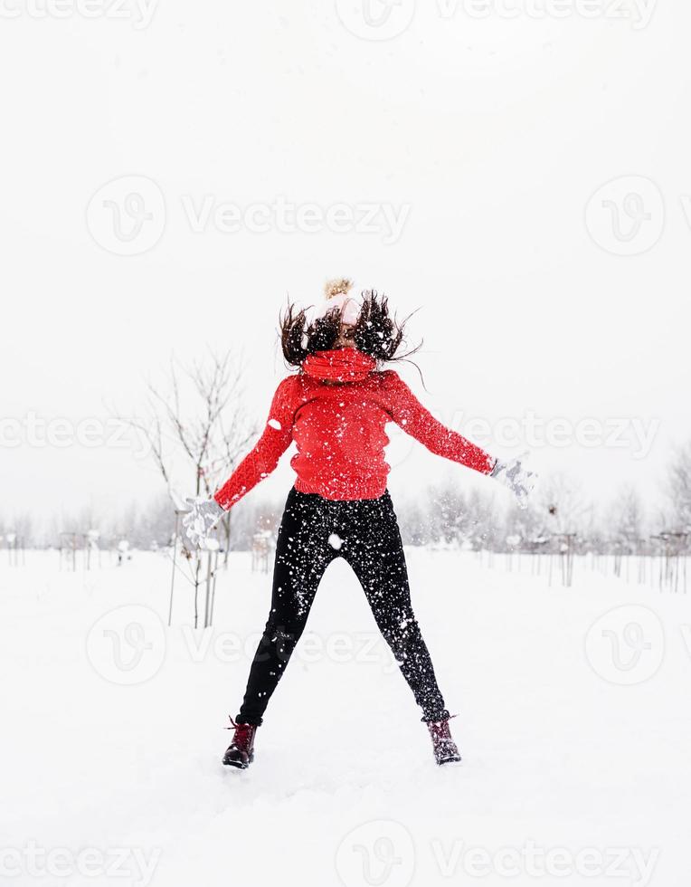 jonge brunette zorgeloze vrouw in rode trui die in de sneeuw buiten springt foto