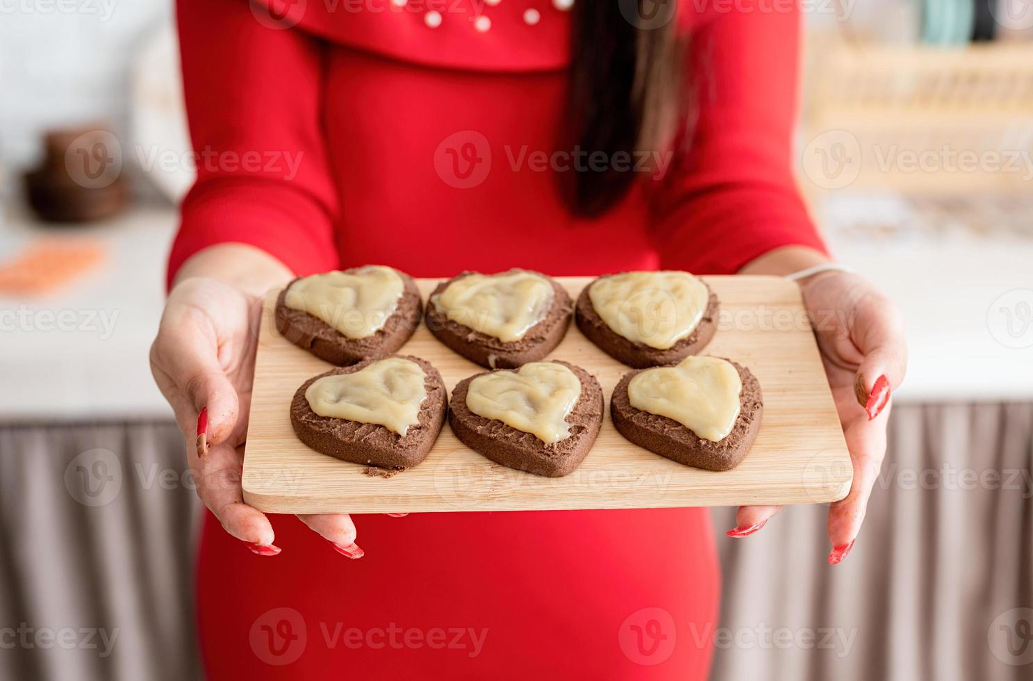 vrouw in rode jurk die valentijnkoekjes maakt in de keuken foto