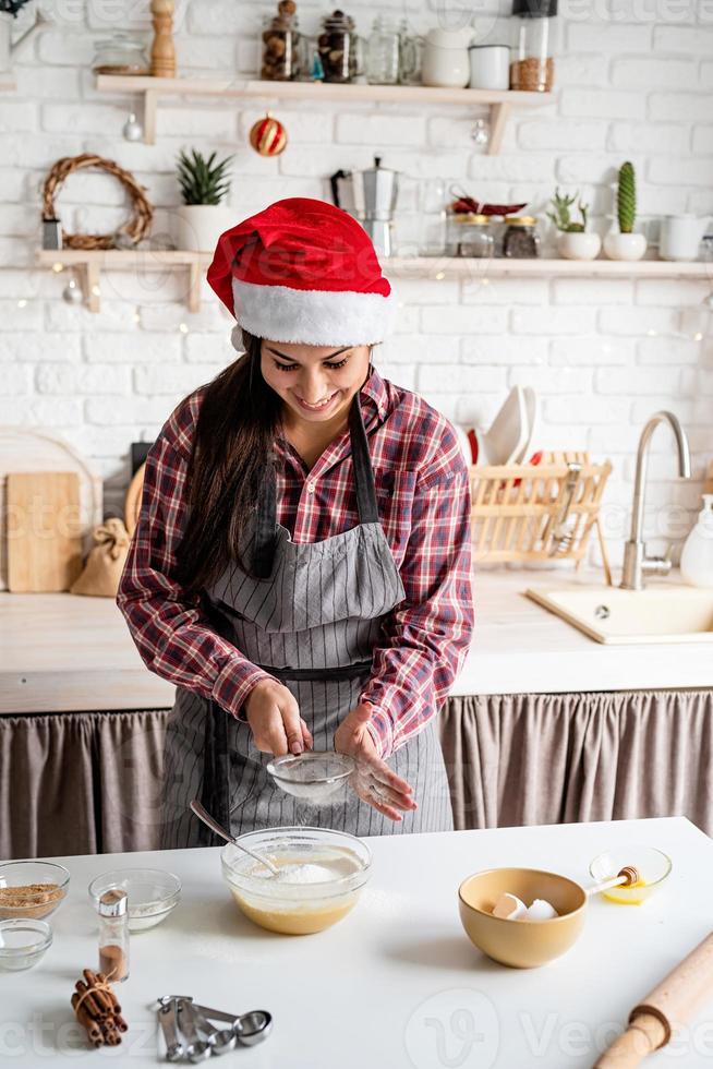 jonge latijnse vrouw die meel giet bij het deeg dat in de keuken kookt foto