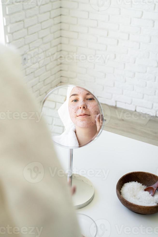 gelukkige jonge vrouw die gezichtsscrub op haar gezicht aanbrengt foto