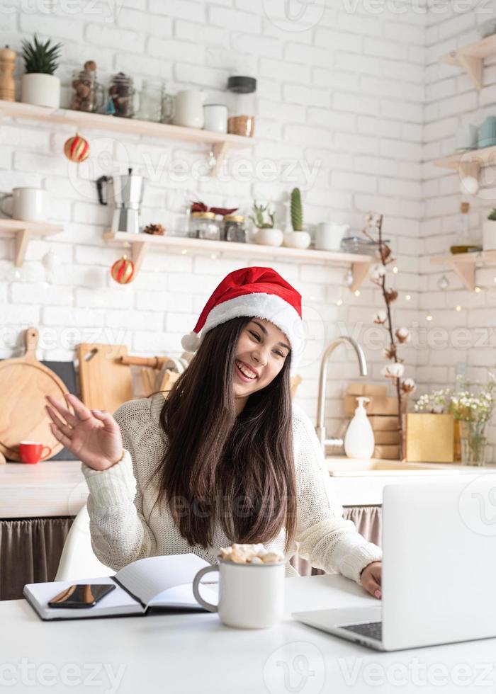 vrouw in kerstmuts chatten met vrienden met behulp van haar laptop foto