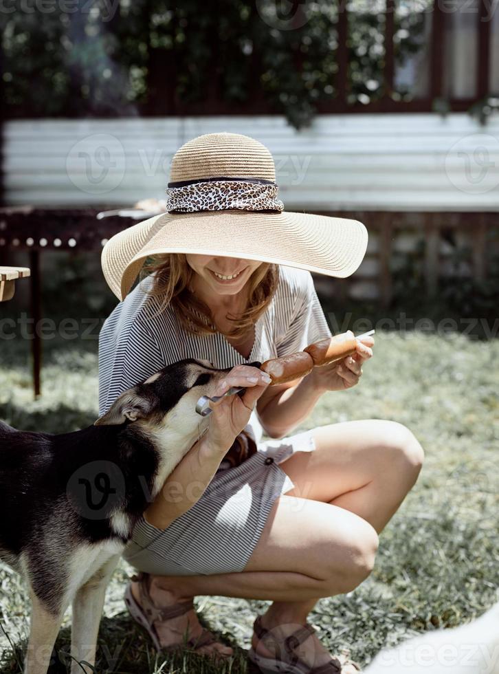 vrouw die vlees buiten in de achtertuin grilt, zittend met haar hond foto