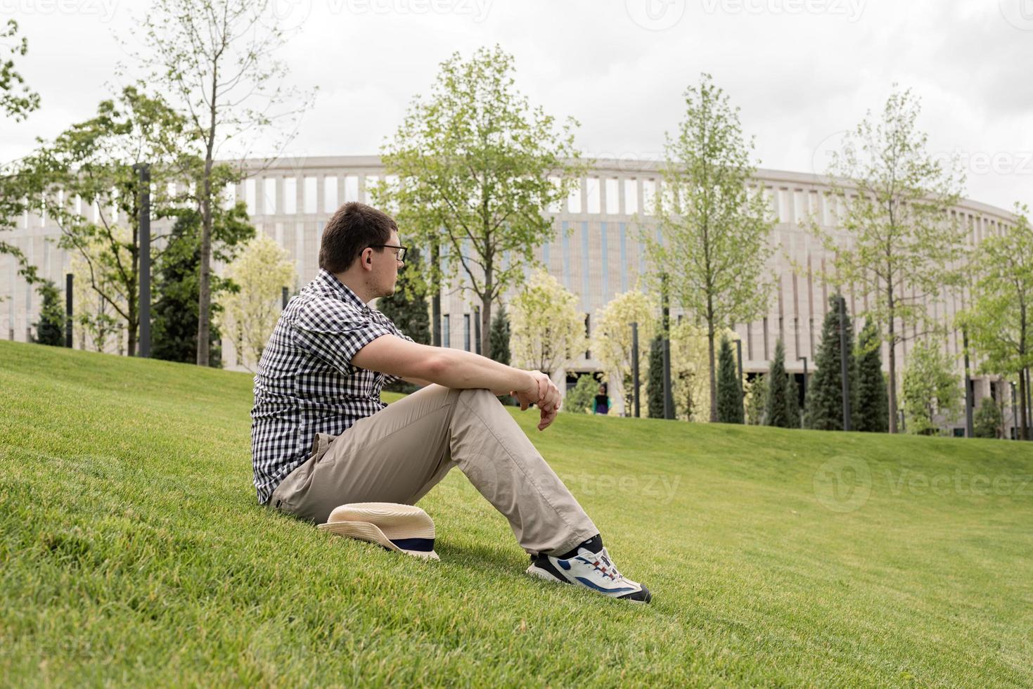 jonge nadenkende man zittend op het gras in het park foto