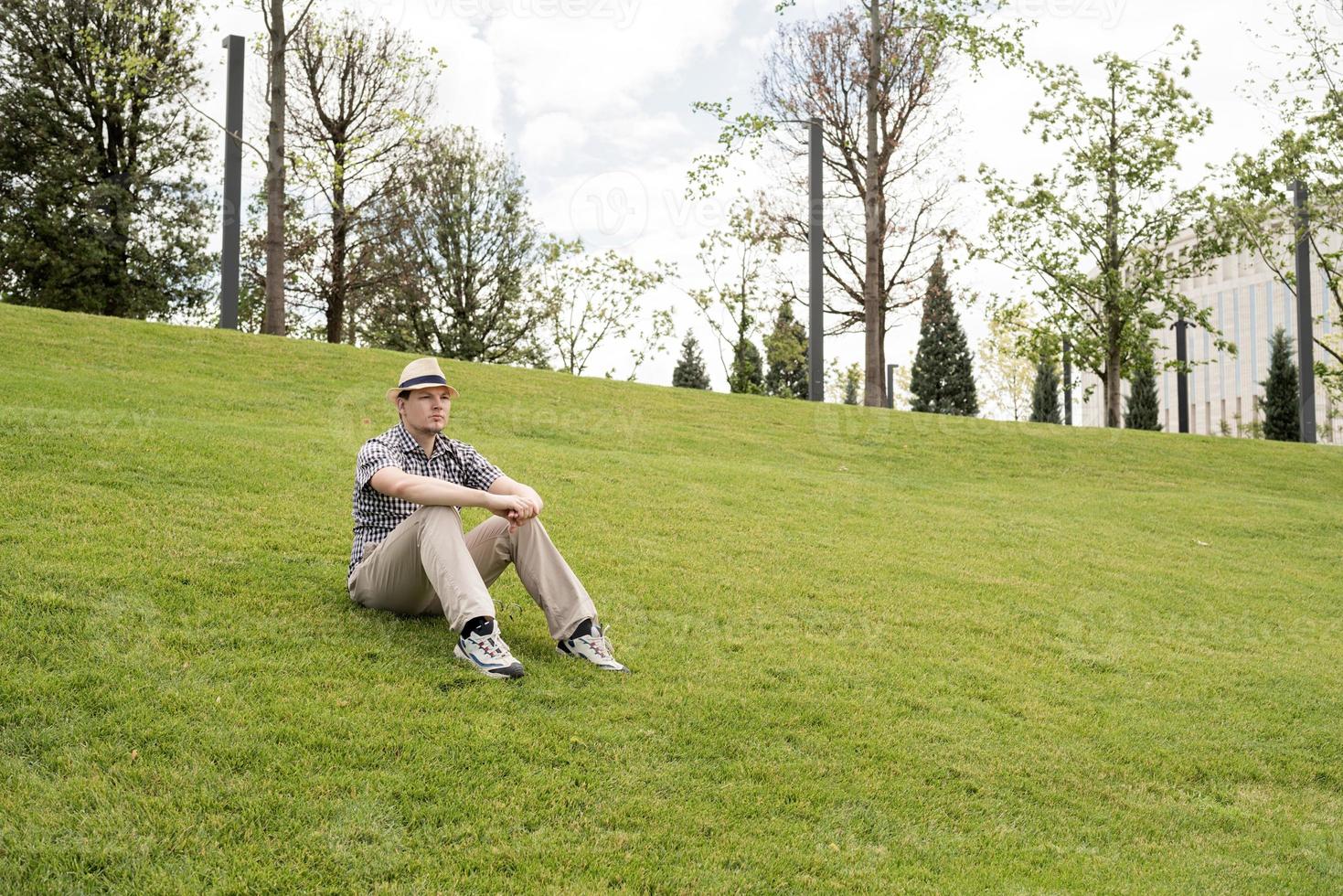 jonge nadenkende man zittend op het gras in het park foto