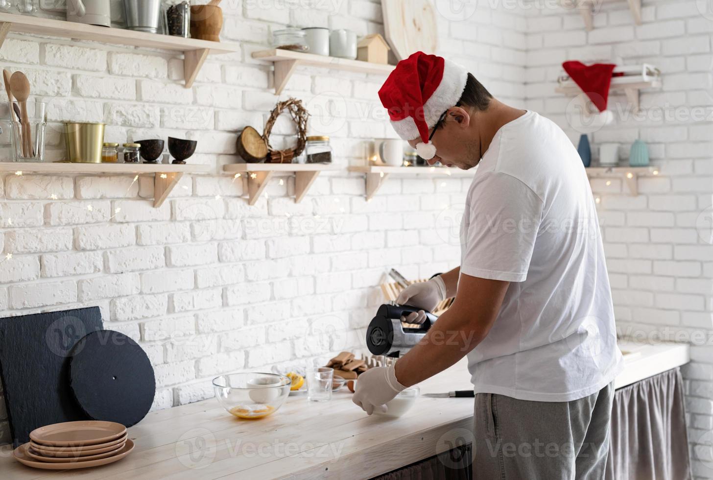 man in kerstmuts die meringue maakt op witte houten tafel foto