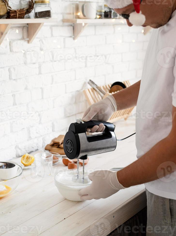 man in kerstmuts die eiwitten opklopt met de elektrische mixer foto