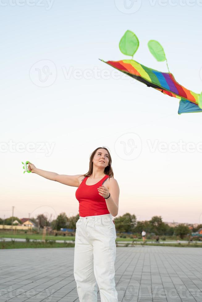 jonge vrouw die een vlieger vliegt in een openbaar park bij zonsondergang foto