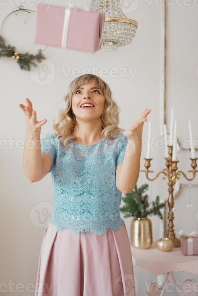 meisje in blauwe blouse en een roze rok werpt een geschenk op en lacht. foto