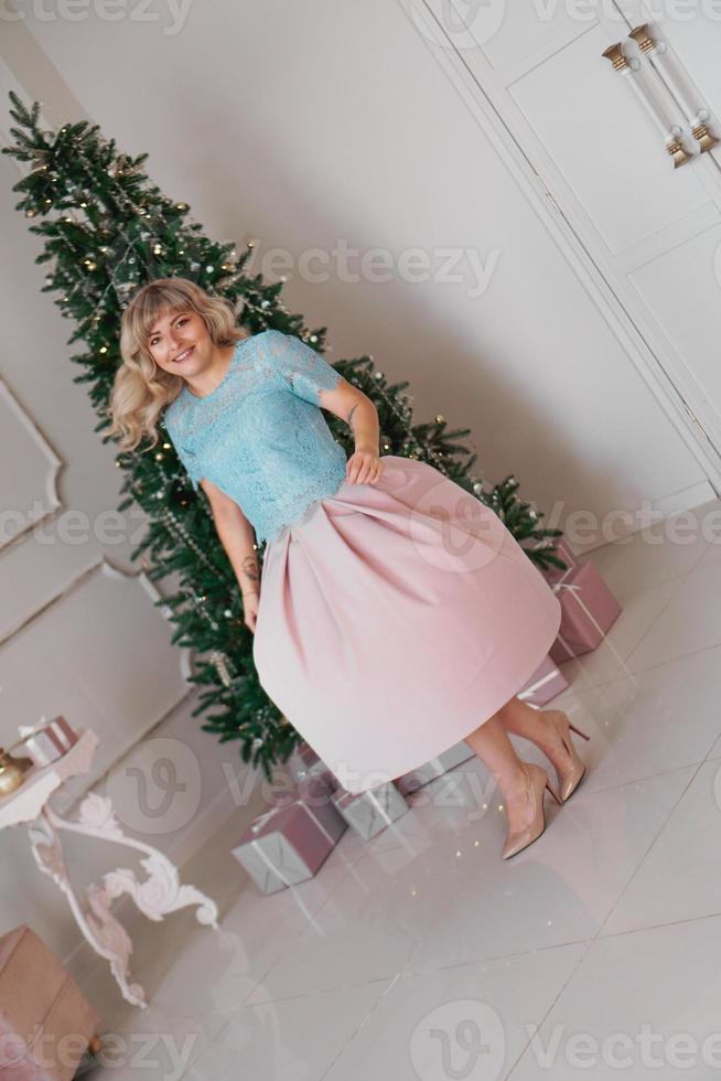 mooie vrouw in de buurt van kerstboom glimlachend dansen in mooie jurk foto