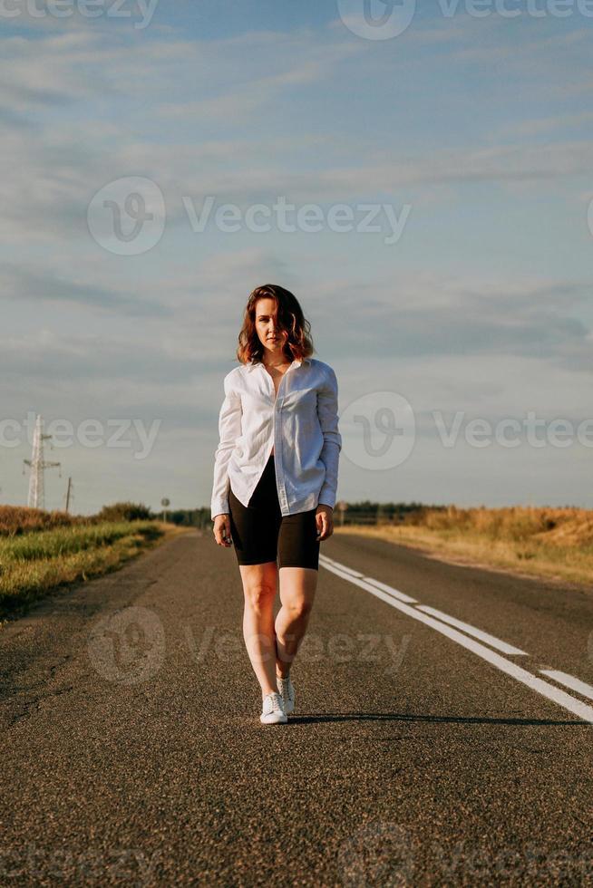 vrouw in een wit overhemd loopt langs de weg tussen de velden foto