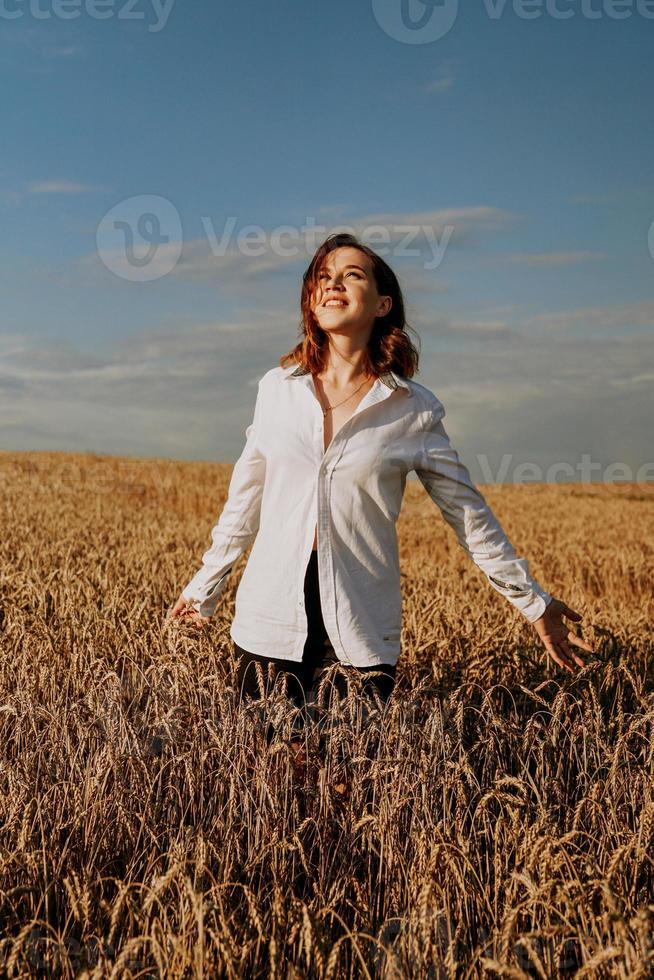 gelukkige jonge vrouw in een wit overhemd in een tarweveld. zonnige dag. foto