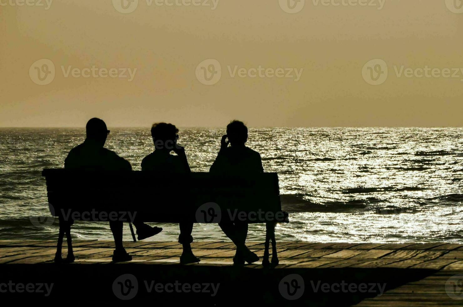 drie mensen zitten Aan een bank met uitzicht de oceaan foto